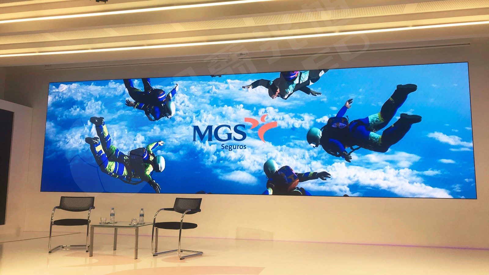 Wide indoor LED video wall above a presentation area with two chairs